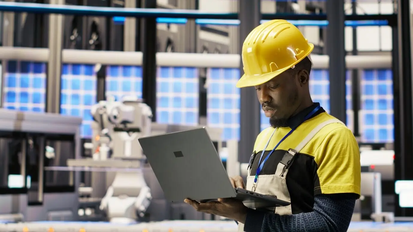 Techniker in einer Solarmodulfabrik überwacht mit einem Laptop Roboter-Montagelinien.