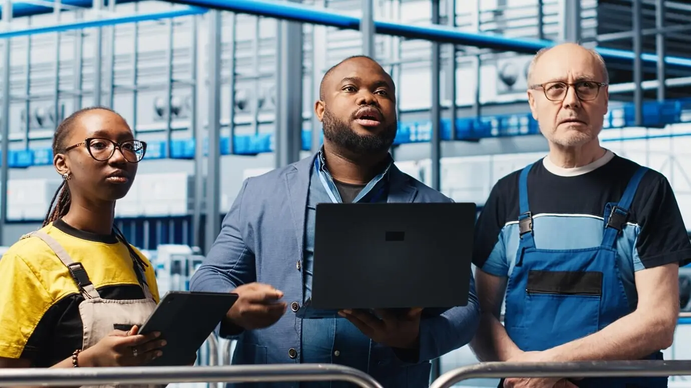 Ein Smart-Factory-Manager bringt Arbeitern bei, Roboterarme mithilfe eines Laptops zu bedienen.